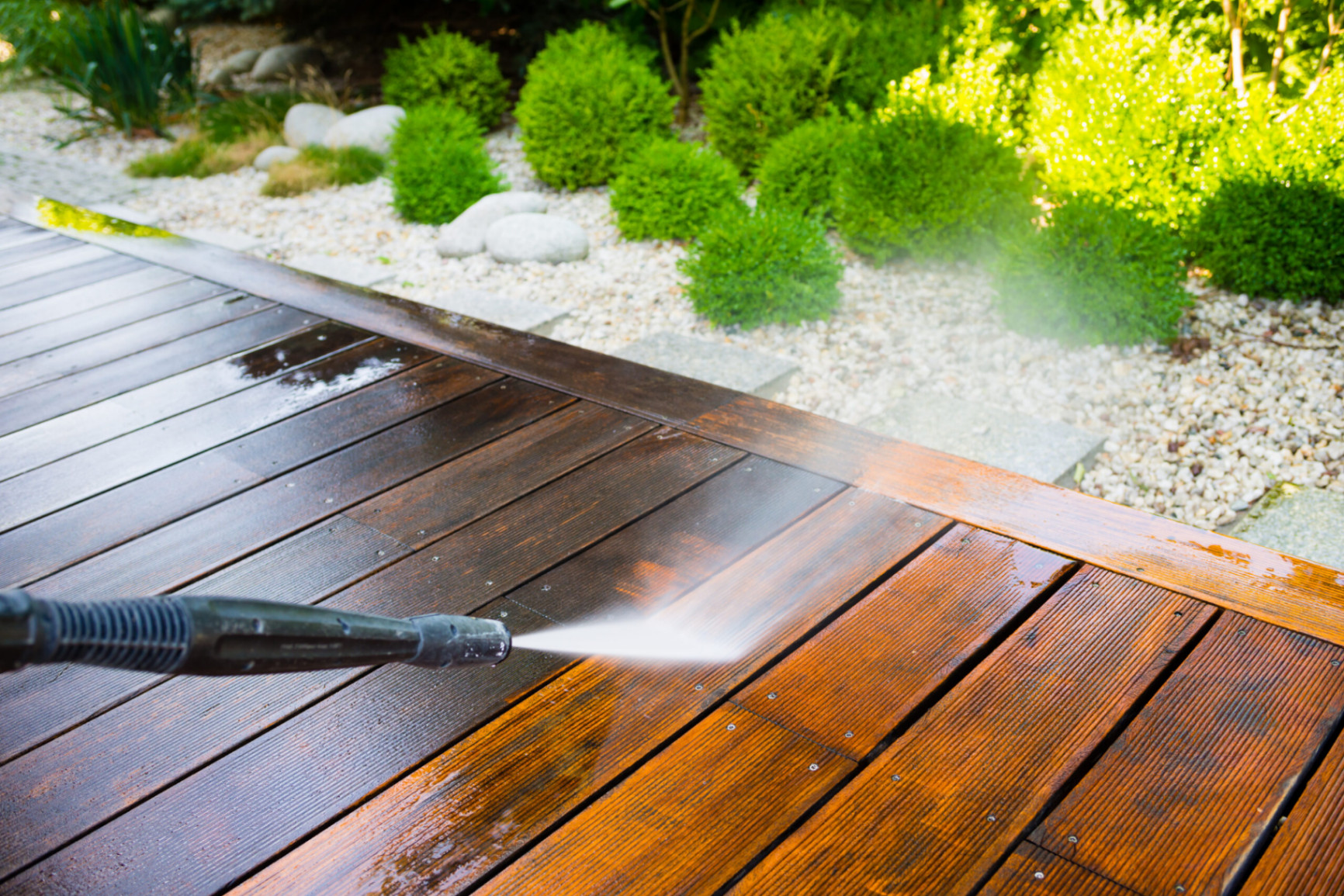 Pressure washing a wooden deck next to landscaped garden